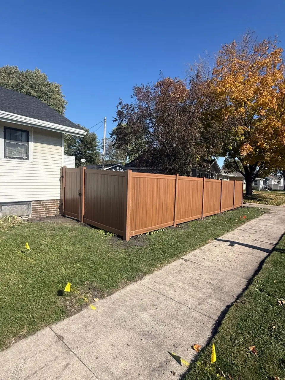 Cedar-tone woodgrain vinyl privacy fence with a matching gate, built by Precision Fence Co.